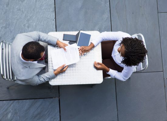 African American businesswoman passing documents to colleague. Two workers reading papers while sitting at table. Business meeting concept